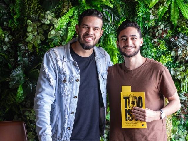 Dois homens seguram o livro juntos no lançamento.